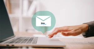 A hand touching the touch pad of a laptop and an envelope icon with a Sales Prophet logo.